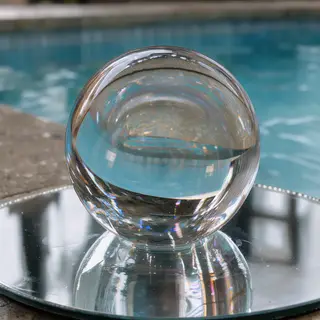 A clear glass sphere sitting on a mirror surface near a pool