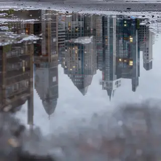 A city skyline reflected in a rain puddle on a street, with 