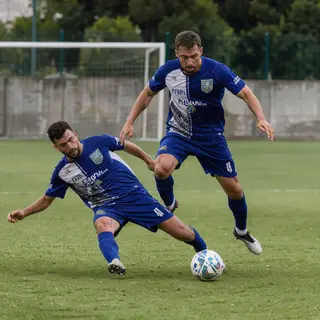 Two soccer players mid-tackle, one sliding and the other jum