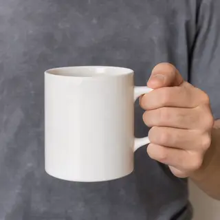 A person holding a white ceramic coffee mug by the handle wi