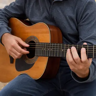 A person playing an acoustic guitar with left hand on the fr