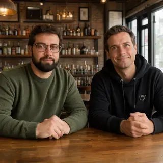 Two men at a cafe: one with a beard and glasses wearing a gr