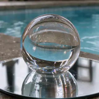 A clear glass sphere sitting on a mirror surface near a pool