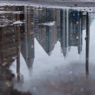 A city skyline reflected in a rain puddle on a street, with 