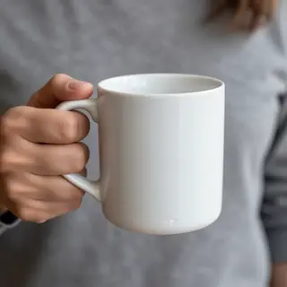 A person holding a white ceramic coffee mug by the handle wi