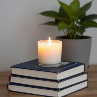 A candle on top of a stack of books, the books next to a pot