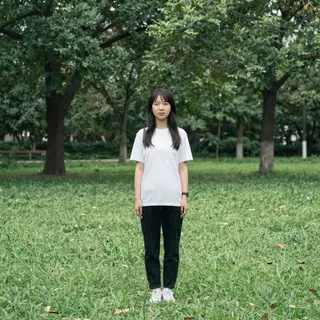 A person standing in a neutral pose in a park, full body vis