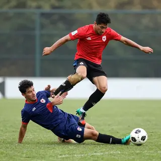 Two soccer players mid-tackle, one sliding and the other jum