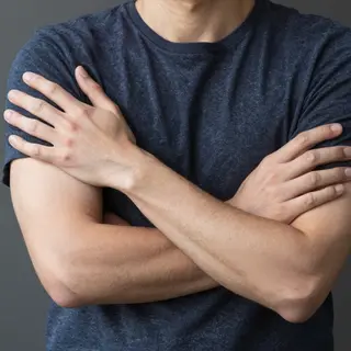 A man with arms crossed, both hands resting on opposite uppe