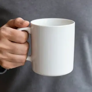 A person holding a white ceramic coffee mug by the handle wi