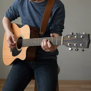 A person playing an acoustic guitar with left hand on the fr