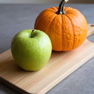 A green apple and an orange pumpkin on a wooden cutting boar