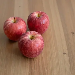 Exactly 3 red apples arranged on a wooden table