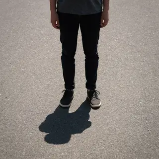 A person standing outdoors at midday with a short shadow dir