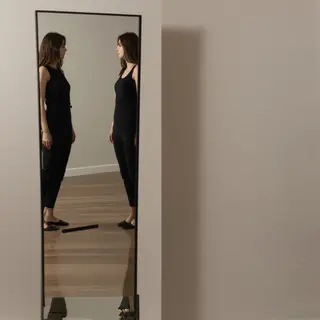 A woman standing in front of a full-length mirror, her refle