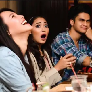 A group of three friends at a table: one laughing with head 