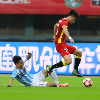 Two soccer players mid-tackle, one sliding and the other jum