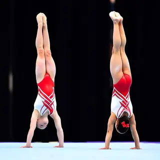 Two gymnasts performing a synchronized handstand, side by si