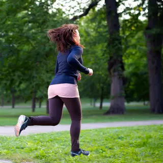 A woman mid-stride running through a park, hair and clothes 
