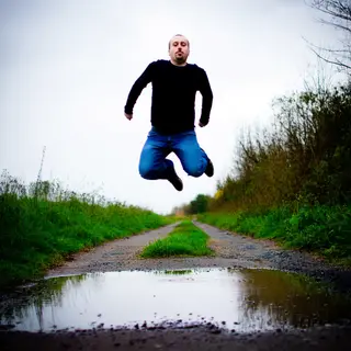 A man captured mid-jump over a puddle, body in the air with 