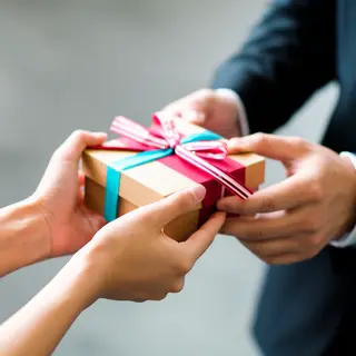 One person handing a small gift box to another person, both 