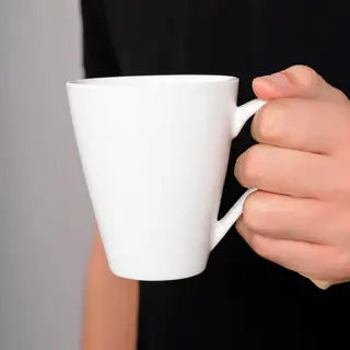 A person holding a white ceramic coffee mug by the handle wi