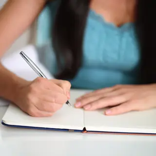 A woman writing in a notebook with a pen gripped correctly i