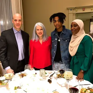 Four people at a dinner table: a bald man in a suit, a woman