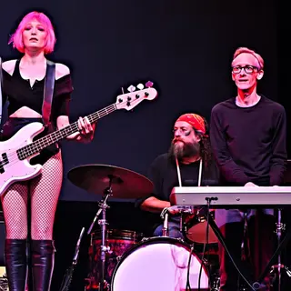 Three musicians on stage: a tall woman with short pink hair 