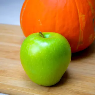 A green apple and an orange pumpkin on a wooden cutting boar