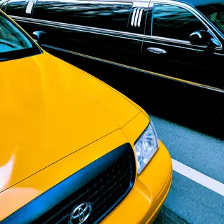 A yellow taxi and a black limousine parked next to each othe