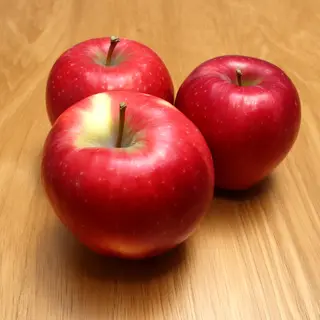 Exactly 3 red apples arranged on a wooden table