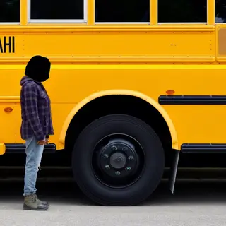 A person standing next to a yellow school bus, showing reali