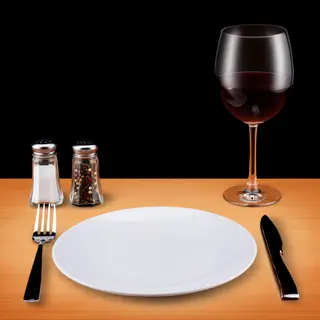 A dinner table scene with a plate, fork, knife, wine glass, 