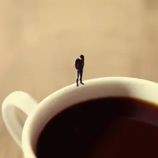 A tiny person standing on the rim of a coffee cup, looking d