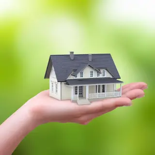 A miniature house sitting on the palm of someone's hand