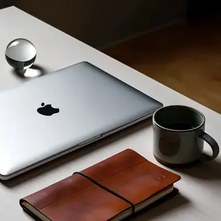 A workspace desk with a brushed aluminum laptop, a leather-b