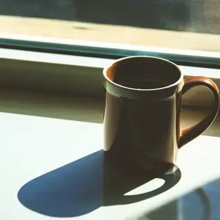 A coffee mug on a sunny windowsill casting a sharp shadow to