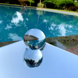 A clear glass sphere sitting on a mirror surface near a pool