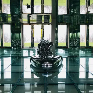 A chrome sculpture in a room with a glass floor and large wi