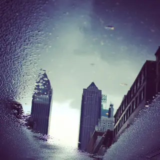 A city skyline reflected in a rain puddle on a street, with 