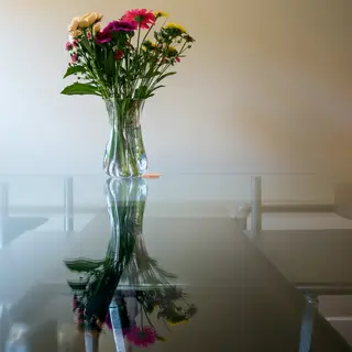 A vase of flowers on a glass table with a clear reflection v