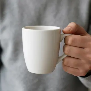 A person holding a white ceramic coffee mug by the handle wi