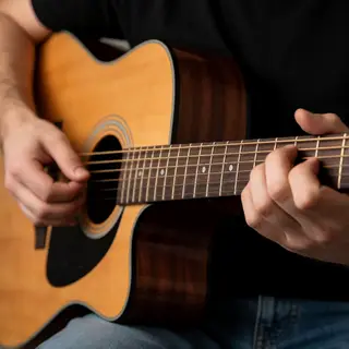 A person playing an acoustic guitar with left hand on the fr