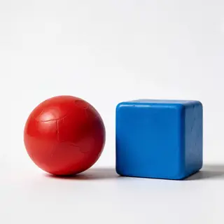 A red ball and a blue cube sitting side by side on a white s