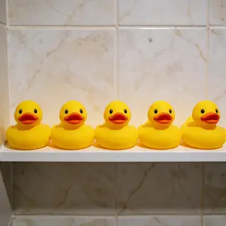 Exactly 5 yellow rubber ducks sitting in a row on a bathroom