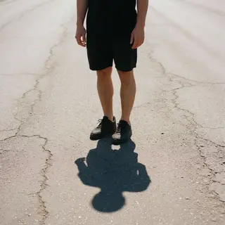 A person standing outdoors at midday with a short shadow dir