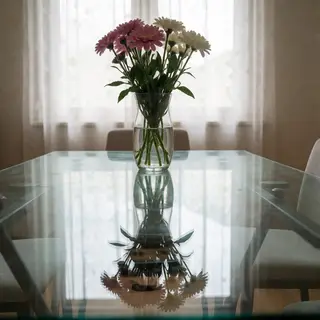 A vase of flowers on a glass table with a clear reflection v