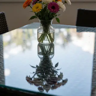 A vase of flowers on a glass table with a clear reflection v