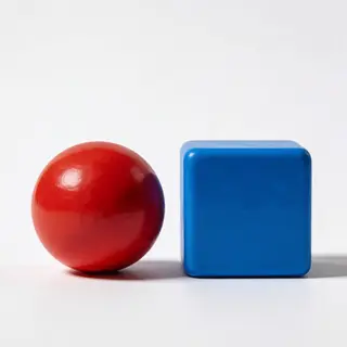 A red ball and a blue cube sitting side by side on a white s